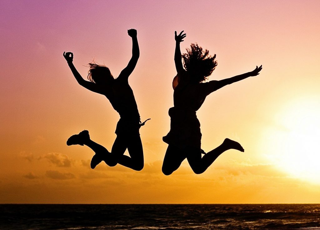 Three people are silhouetted, jumping in the air on a sunset beach over the ocean, expressing joy.